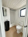 Sawmill Structures Wanderlove Tiny Home bathroom includes a white toilet, tall black sink, walk-in shower, and a window for natural light
