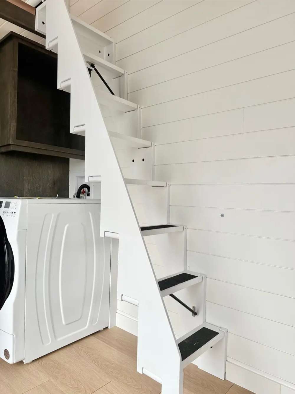 Sawmill Structures Wanderlove Tiny Home includes a compact white staircase with dark step grips and a washer-dryer