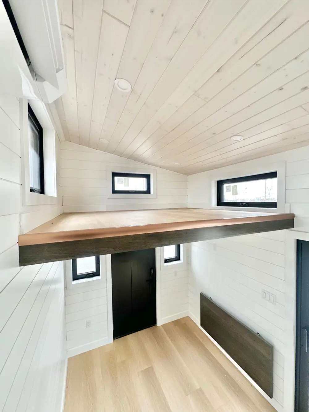 Sawmill Structures Wanderlove Tiny Home includes a loft space above the entrance with white shiplap walls, light wood flooring, and several windows