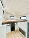 Sawmill Structures Wanderlove Tiny Home includes a loft space above the entrance with white shiplap walls, light wood flooring, and several windows