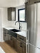 Sawmill Structures Wanderlove Tiny Home kitchen shows a modern black sink, marble-style counter, stainless fridge, and matching dark cabinets