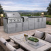 Scenic outdoor view of the Sunstone Magnolia 10ft Outdoor Kitchen Island Package with grill, sink, and cabinets near dining area