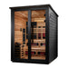 Seen from the front right, Golden Designs Kaskinen 6 Person Black Barn Hybrid Outdoor Sauna shows its black exterior, glass doors and guarded stove inside