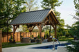 Set against lush greenery, the Brookside Timber Frame Alpine Lodge Pavilion blends rustic elegance with modern outdoor living in a tranquil backyard setting