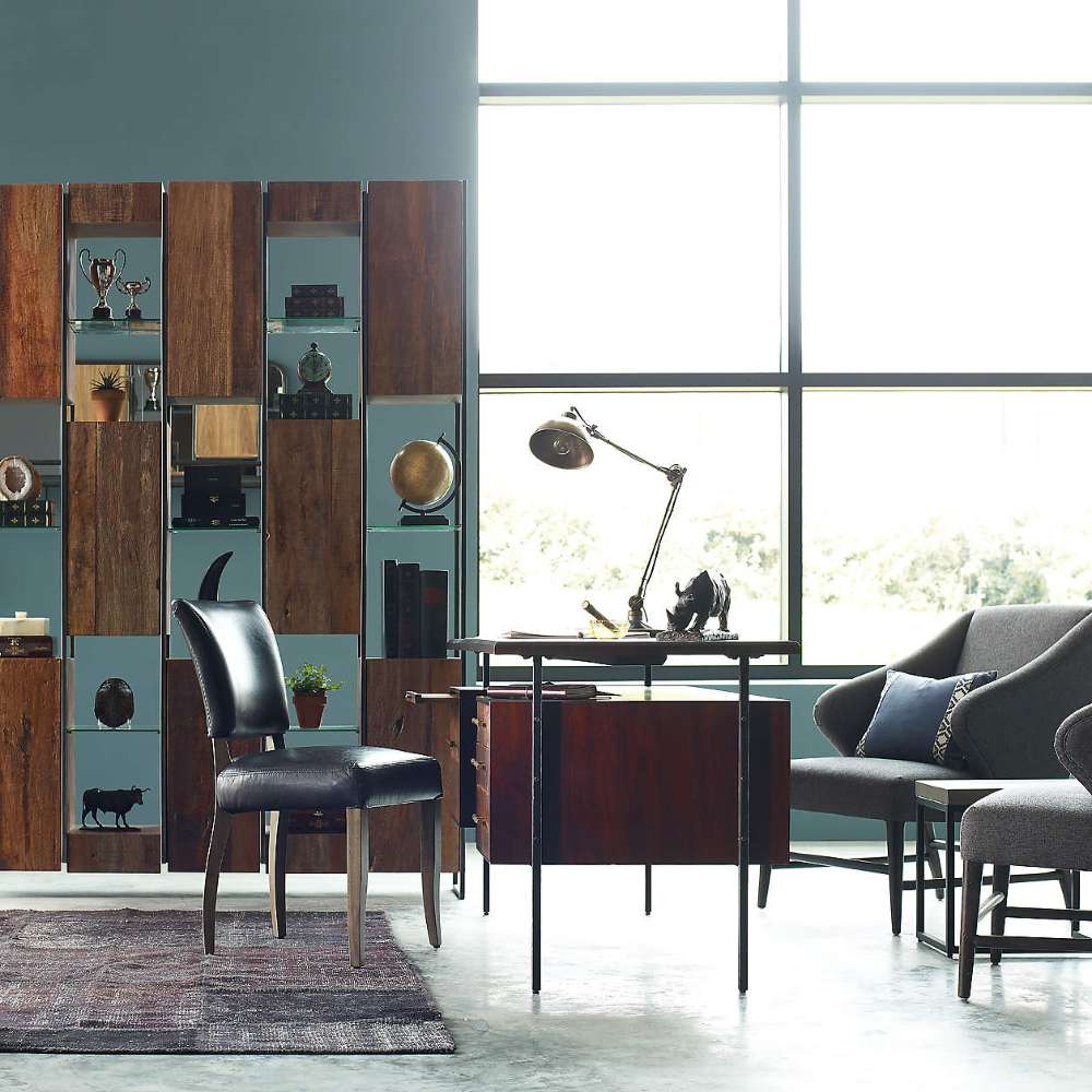 Set in a modern office, Crate & Barrel Sedgwick Solid Acacia Wood Desk with Storage is paired with a black chair, lounge seating, and tall shelving