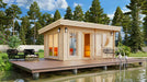 Set in a lush garden, the GardenHouse24 USA Sauna Sahib 70 Garden Room features large windows, warm lighting, and a round wooden wall detail, creating a peaceful retreat