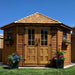 Set against a bright blue sky, the Outdoor Living Today 9×9 Penthouse Garden Shed showcases cedar woodwork and blooming flower boxes
