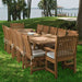 Several Westminster Teak Veranda Teak Armchairs are arranged around a large table on grass near palm trees and a lake, forming a spacious outdoor dining area