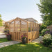 Side angle view shows the 8x8 Outdoor Living Today Western Red Cedar Greenhouse Kit surrounded by flowers and greenery