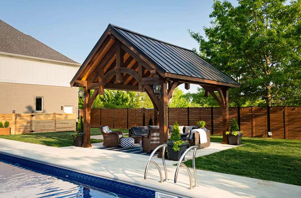 Side view of Brookside Timber Frame Alpine Lodge Pavilion highlights its sturdy wooden beams and luxurious outdoor furniture