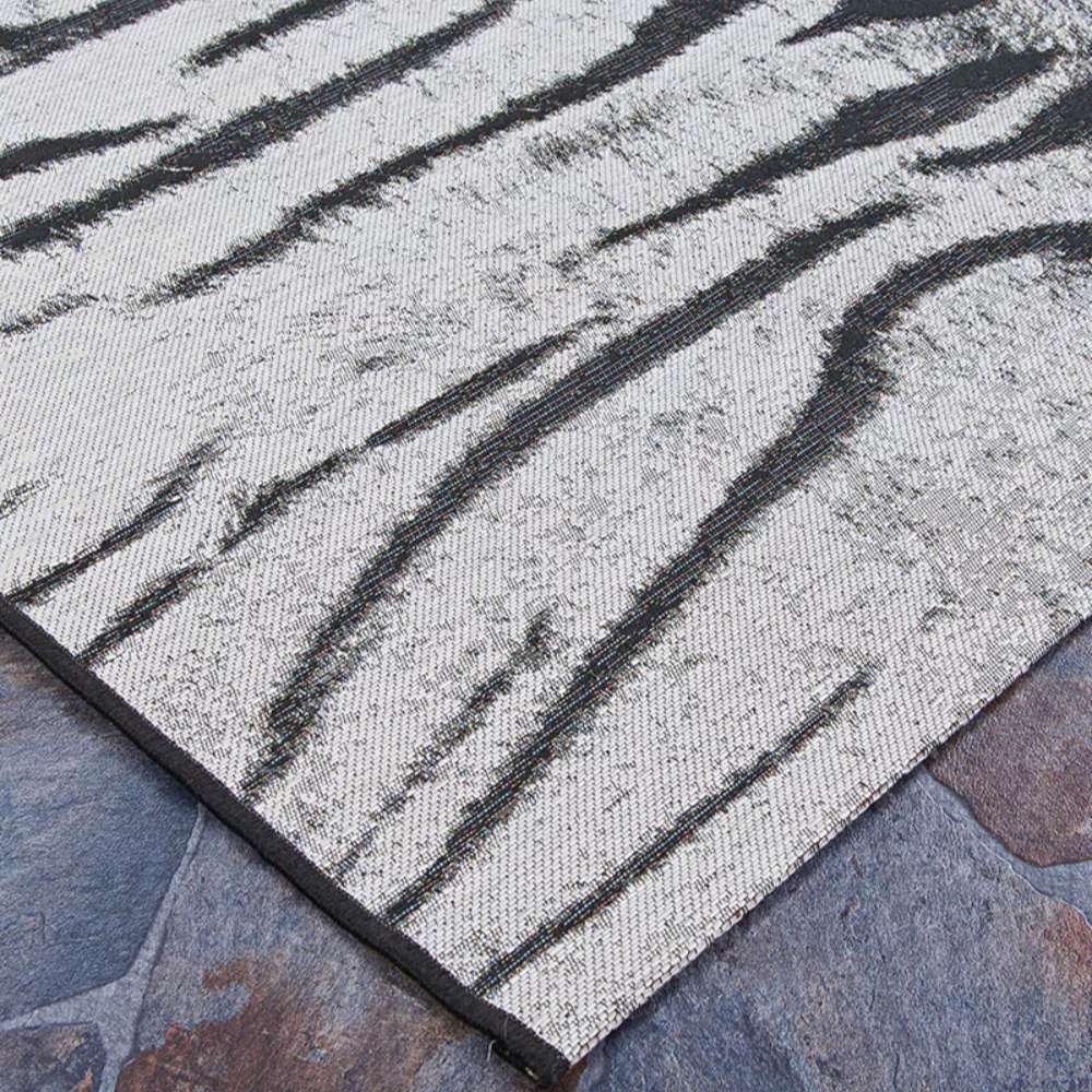 Side view of Couristan Dolce Indoor/Outdoor Rug - Bengal/Ivory lying flat on stone tiles