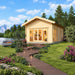 Sigrid 44 wooden garden room in a landscaped lakeside setting, featuring glazed doors, warm interior lighting, an illuminated walkway, flowers, pine trees and distant mountains.