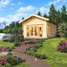 Sigrid 70 wooden garden room with broad glazed doors and warm interior lighting, surrounded by flowers and an illuminated walkway beside a lake with boats, pine trees and mountains.