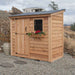 Single Door Metal Roof Outdoor Living Today 8×4 SpaceSaver Lean-To Cedar Shed is set on gravel with a slanted metal roof, front window with flowers, and vertical plank door under cloudy skies