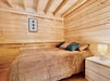 Snug bedroom in the Sawmill Structures Edwin Lake House PLUS 70MM Garden Room features wood-paneled walls, a slanted ceiling, a soft beige bedspread, and a small nightstand with a lamp