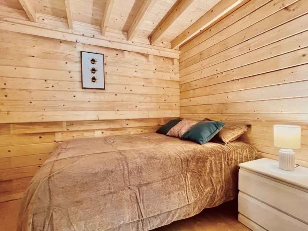Snug bedroom with a queen-sized bed, side table, and lamp sits tucked in the Sawmill Structures Edwin Lake House 70MM Garden Room