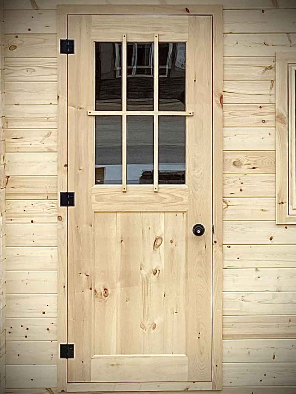 Solid wooden door with a vertical window grid design on the exterior of the Sawmill Structures Harvest Grand Bungalow 107 Garden Room