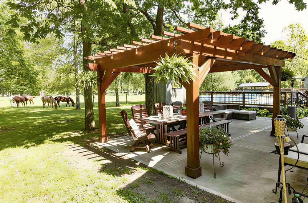 Spacious backyard patio with Brookside Timber Frame Shadelan Retreat Pergola shading a wooden dining set under trees, creating a relaxing outdoor seating area