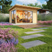 GardenHouse24 USA Starla 44A ALU Garden Room is pictured in a landscaped backyard setup, used as an office space with visible desk, flowers, and artwork inside