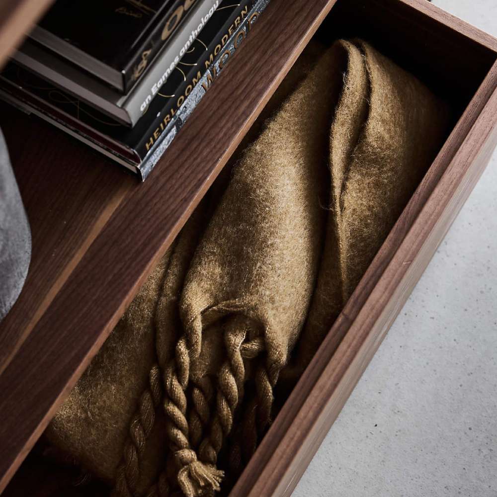 Storage drawer detail of Crate & Barrel Siena 34" Walnut Wood 4-Shelf Storage Bookcase with Drawer holding a folded throw blanket
