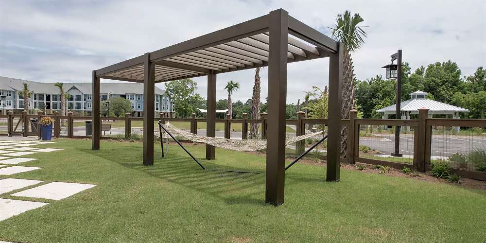 Structureworks Stratus Aluminum Pergola stands over a hammock in a grassy yard near palm trees and a wooden fence