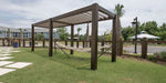 Structureworks Stratus Aluminum Pergola stands over a hammock in a grassy yard near palm trees and a wooden fence