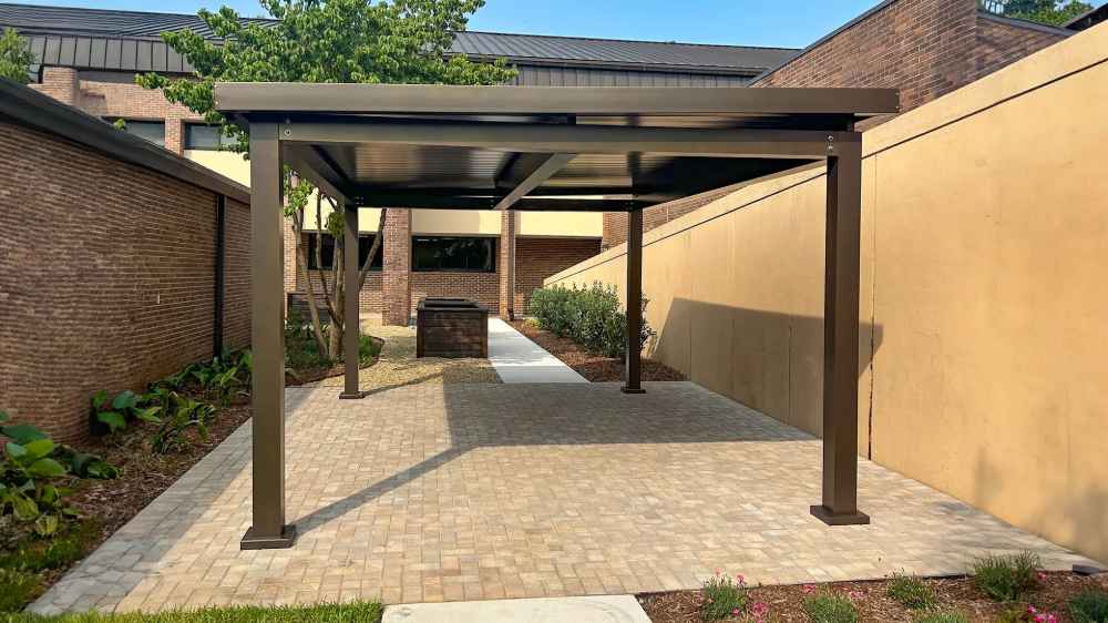 Structureworks Pavilion Trex Pergola stands on a paved walkway between two brick buildings