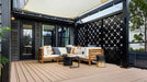 Structureworks Solis Trex Pergola shades an urban courtyard lounge area with wooden outdoor furniture and potted plants
