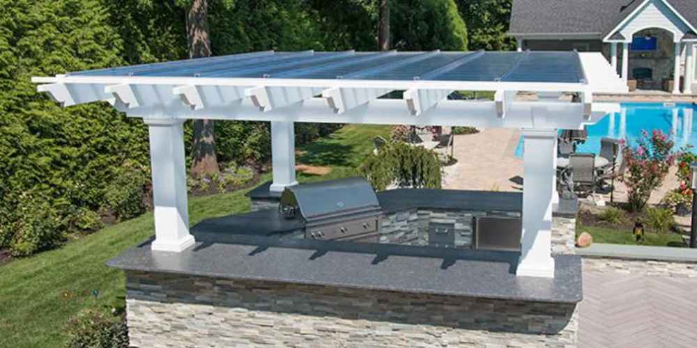 Structureworks Williamsburg Fiberglass Pergola with a clear roof panel shelters an outdoor kitchen island by the pool