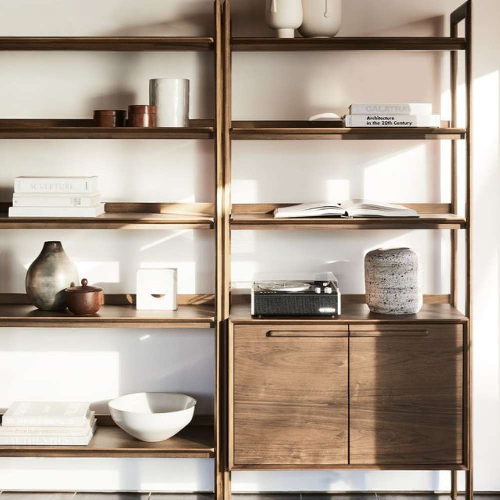 Sunlit display of Crate & Barrel Tate 36" Walnut Wood 3-Shelf Storage Bookcase Cabinet styled with books, ceramics, and décor on open shelves above closed cabinet storag