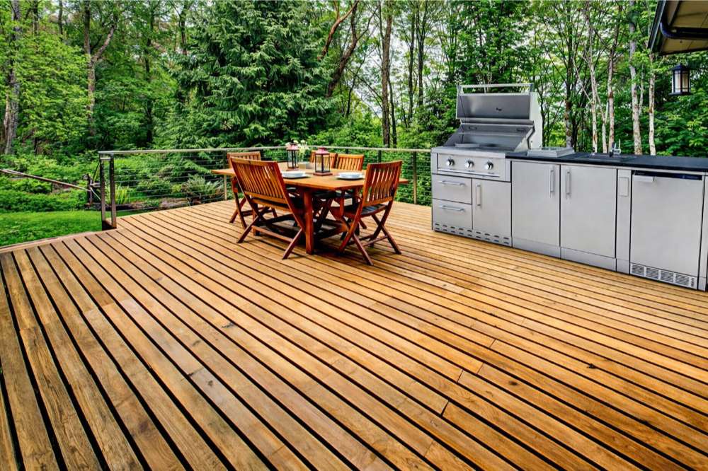 Sunstone Bayou 8ft 6in Outdoor Kitchen Island Package on a wooden deck with grill, cabinets, and outdoor dining setup
