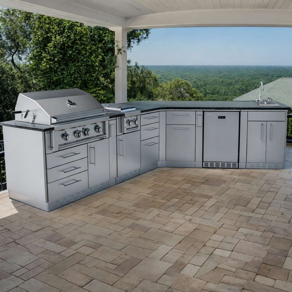 Sunstone Savanna 16ft Outdoor Cabinet Package with 60° Angle is a stainless steel outdoor kitchen with grill and sink on a covered patio overlooking a forest