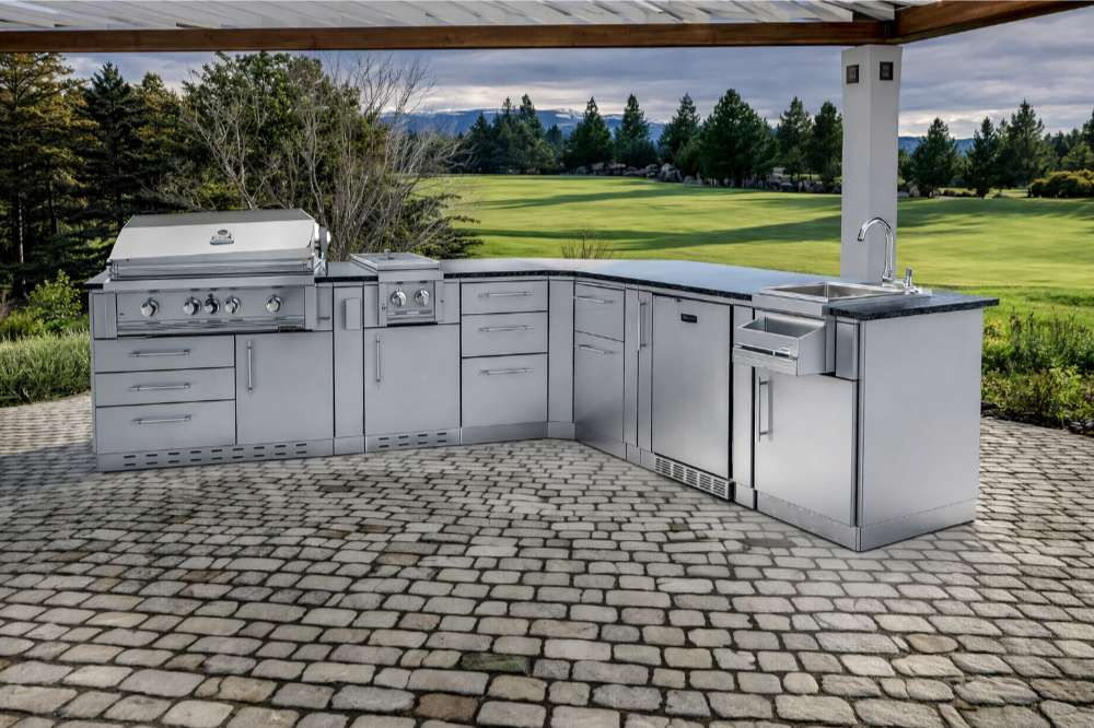 Sunstone Savanna 16ft Outdoor Cabinet Package with 60° Angle sits on a stone patio with a grill, burner, fridge, and sink facing a scenic golf course