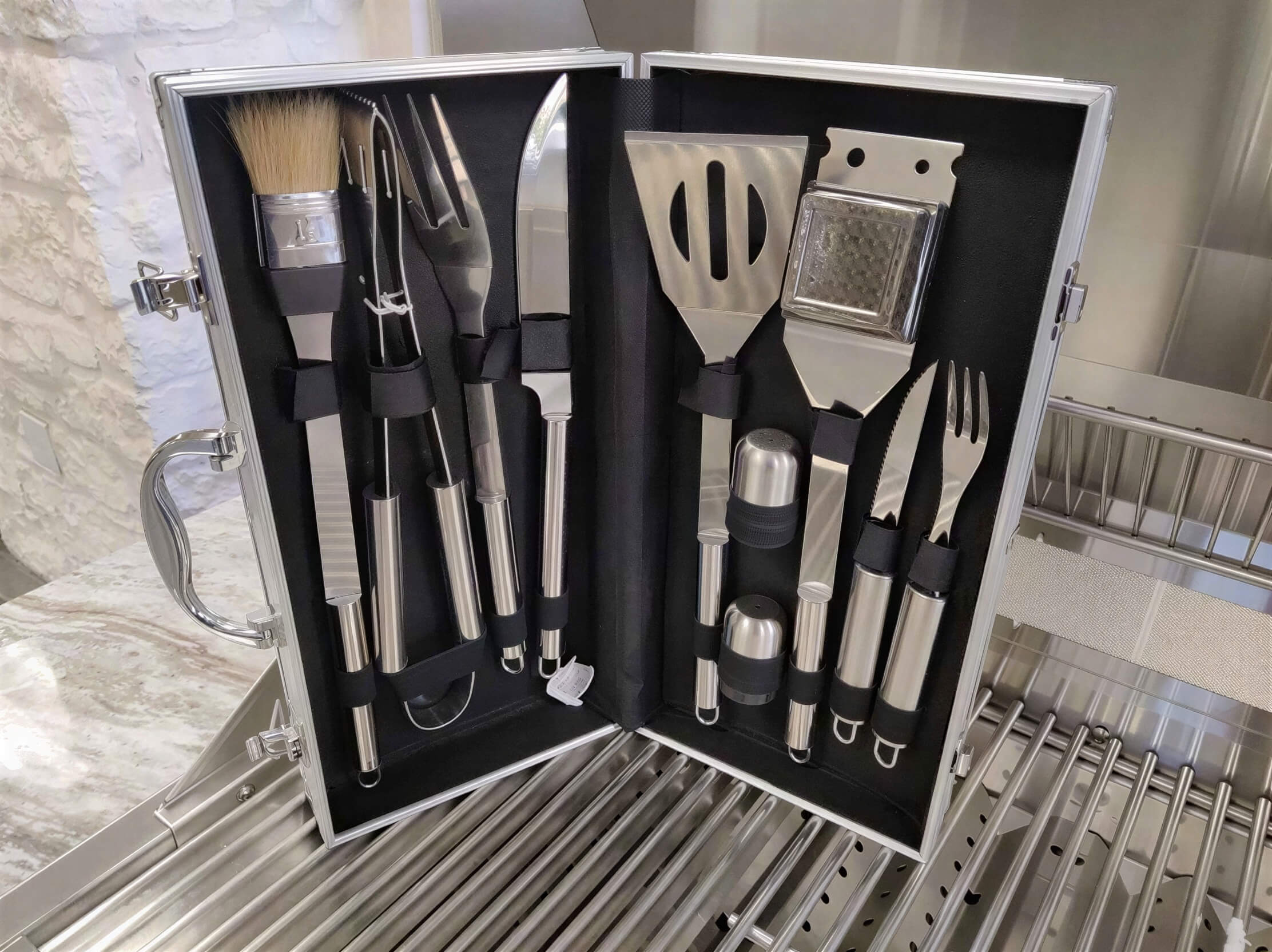 Sunstone 10 Piece Stainless Steel BBQ Tool Set w Carry Case is opened on a grill, showing neatly arranged tools including a spatula, tongs, knives, and basting brush