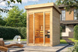 Surrounded by trees and sunshine, Sawmill Structures TS TwoSauna Sauna stands elegantly with its sleek, vertical wood design and inviting glass-front entrance