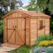 Surrounded by lush flowers, the Outdoor Living Today 8×12 Space Master Storage Shed has a shingled roof and flower box under a side window