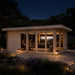 Rectangular wood cabin with glass doors at night, showing people watching a screen inside the illuminated Taunus 70 suite.