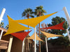 Tenshon Right Triangle Shade Sail installed in overlapping bright yellow, red, and tan panels above an outdoor courtyard