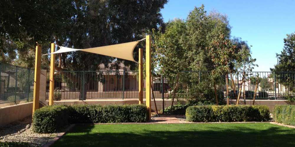 Tenshon Square Shade Sail is mounted on wooden posts to create shade over a landscaped garden walkway
