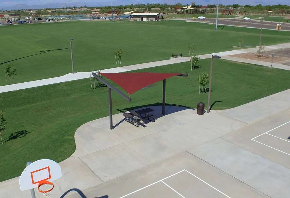 Tenshon Square Shade Sail provides shaded seating over a picnic table near a basketball court in a spacious community park