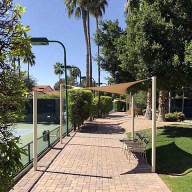 Tenshon Square Shade Sail stretches above a tennis court walkway, creating comfortable shade for benches beneath palm trees