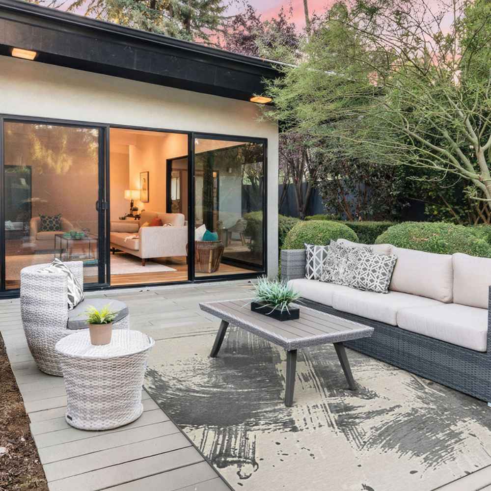 The Couristan Castille Indoor/Outdoor Rug - Canvas/Glacier lies under outdoor furniture on a stylish patio