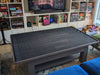 The Game Theory Tables The Origins Coffee Table with a spacious dark playing surface, set in a game room surrounded by board games and shelves