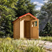 Angled view of The Wee Wee House 33 with an open windowed door, red gabled roof and natural wood interior amid tall grasses and leafy trees.