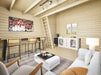 The bright interior of the Sawmill Structures BlueWater Loft 160 70mm Garden Room includes a bar table, loft access, and comfortable furnishings