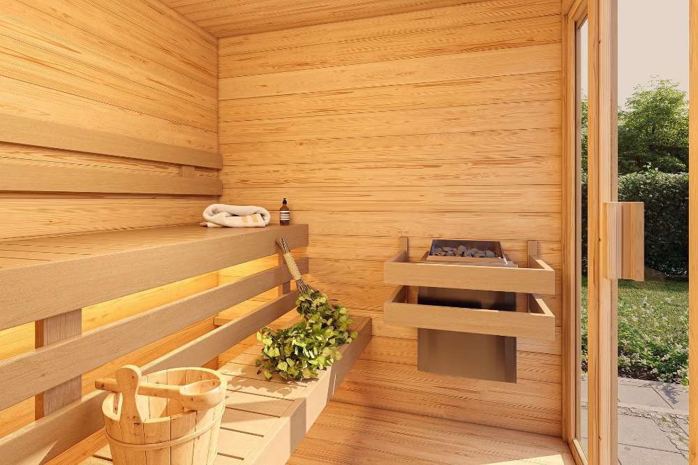 The interior of Sawmill Structures TS TwoSauna Sauna reveals clean wooden lines, a bucket and ladle, sauna stones, and natural light