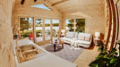The kitchen sink and counter of the Sawmill Structures Edwin Lake House 70MM Garden Room face a bright and airy living room with large windows and comfy seating