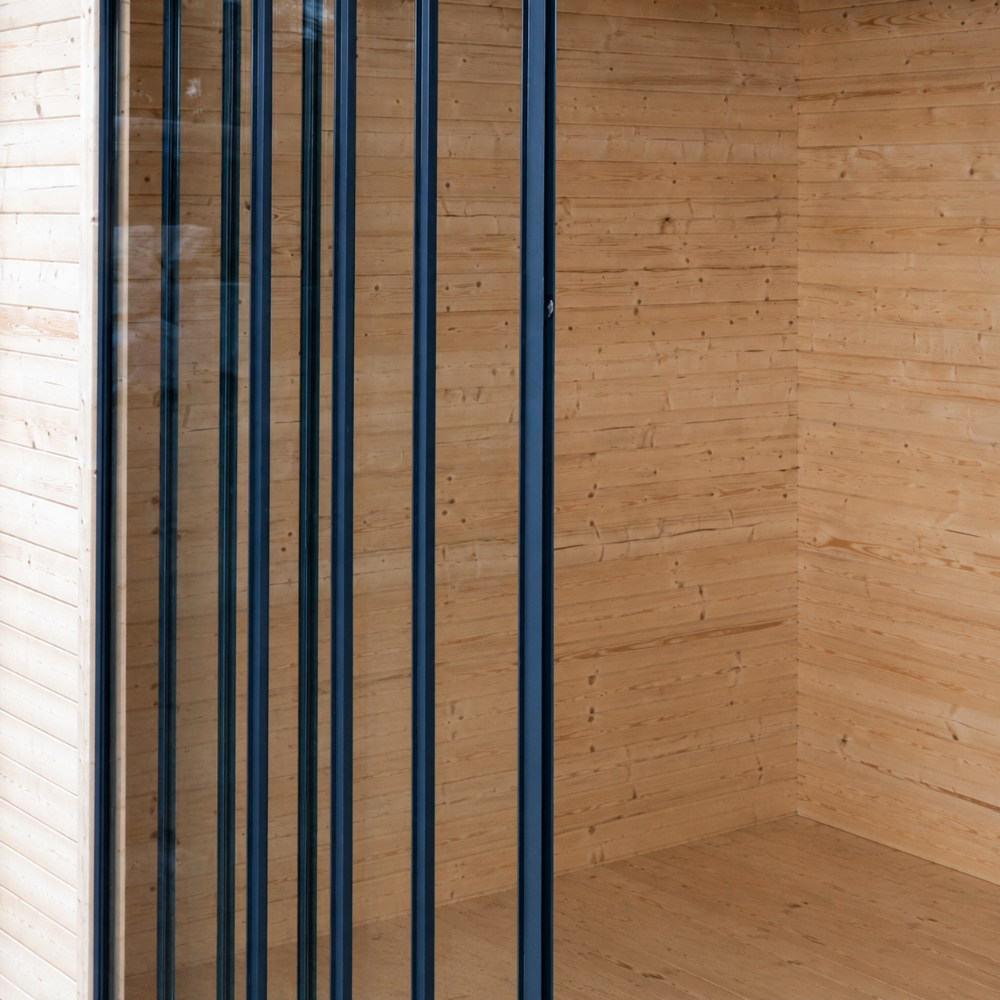 The tall, vertical glass panels of the GardenHouse24 USA ALU Concept 44Q Garden Room are neatly aligned in a wooden wall