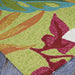The corner of the Couristan Covington Indoor/Outdoor Rug - Painted Fern/Fern-Red rests on stone flooring
