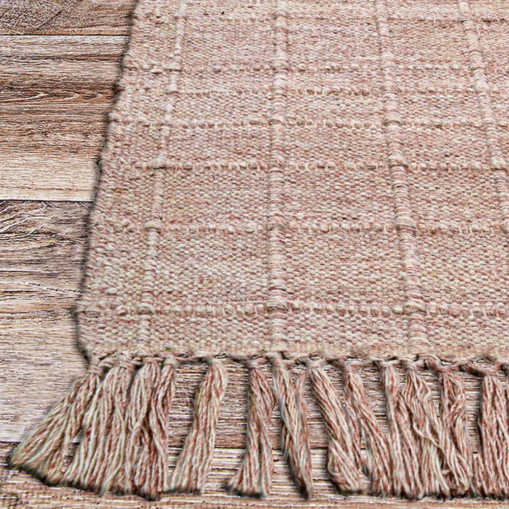 The edge of the Couristan Ascot Indoor/Outdoor Rug - Windowpane/Rose displays thick fringe and a subtle plaid design over a rustic wood floor
